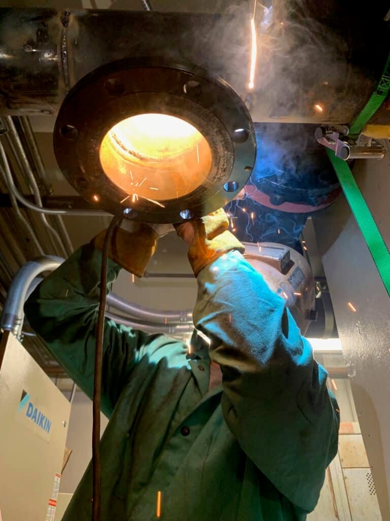 alt="Worker performing an emergency weld on a pipe fitting"